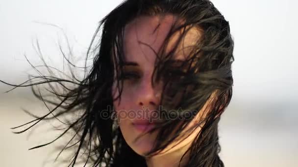Retrato de una hermosa chica sonriendo en la playa al atardecer con el pelo ondulado . — Vídeos de Stock