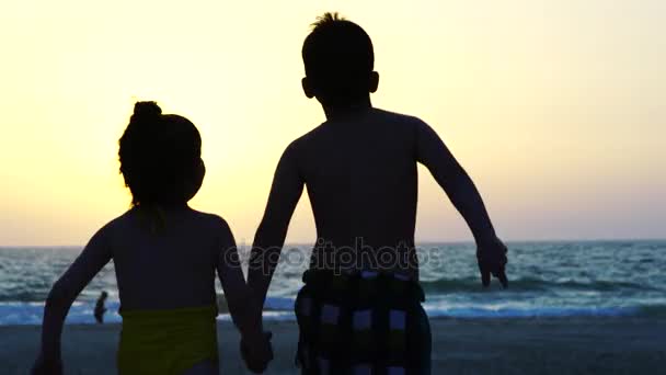 Liten pojke och flicka kör över stranden. — Stockvideo
