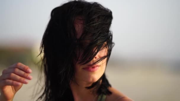 Retrato de una hermosa chica sonriendo en la playa al atardecer con el pelo ondulado . — Vídeos de Stock