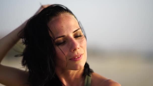 Retrato de una hermosa chica sonriendo en la playa al atardecer con el pelo ondulado . — Vídeo de stock