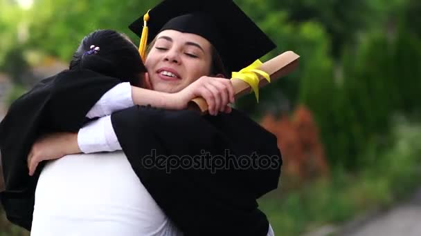 Cena ao ar livre de bela estudante de graduação do sexo feminino vestida com copo e vestido, abraçando seus pais . — Vídeo de Stock