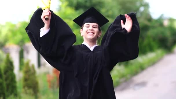 Escena al aire libre de una hermosa estudiante graduada vestida con copa y vestido saltando . — Vídeo de stock