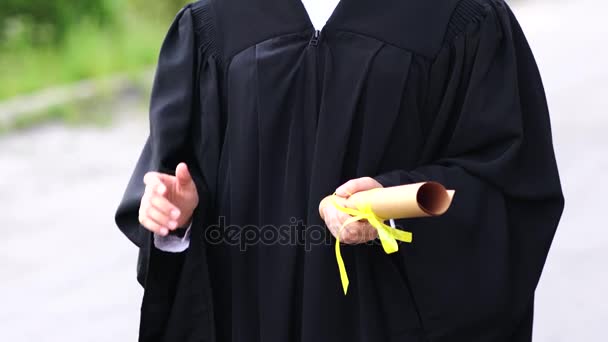 Outdoor scene of beautiful female graduating student dressed in cup and gown. — Stock Video