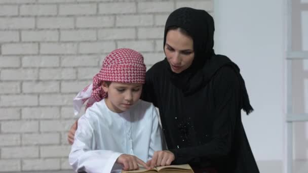 Arabische Mutter und Sohn lesen drinnen. — Stockvideo