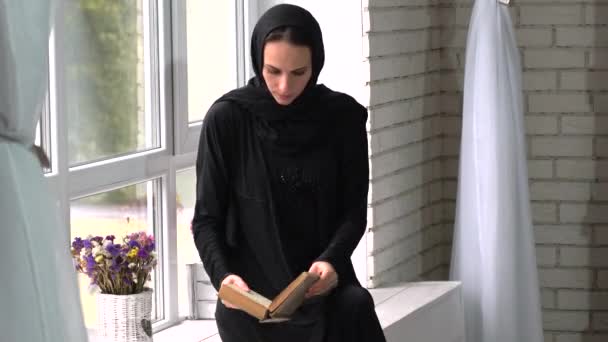 Όμορφη αναμιγνύεται Ανατολική νεαρή γυναίκα διαβάζοντας το βιβλίο δίπλα σε παράθυρο. — Αρχείο Βίντεο