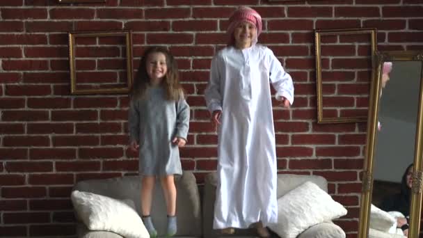 Två arabiska barn hoppa soffan inomhus. — Stockvideo