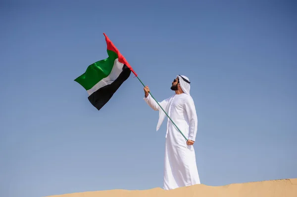 Orgulloso hombre árabe emiratí sosteniendo una bandera de los EAU en el desierto . — Foto de Stock