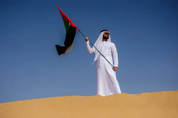 Orgulhoso homem Emirado árabe segurando uma bandeira dos Emirados Árabes Unidos no deserto . — Fotografia de Stock