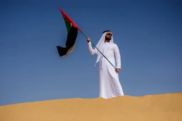 Orgulloso hombre árabe emiratí sosteniendo una bandera de los EAU en el desierto . — Foto de Stock