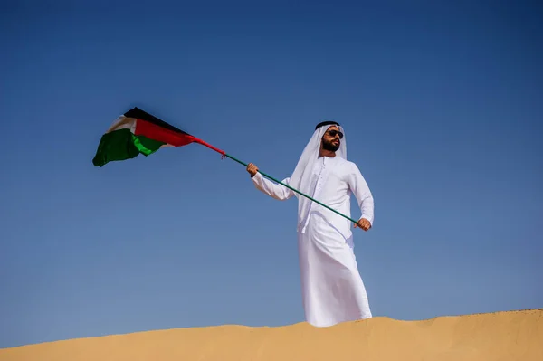 Orgulloso hombre árabe emiratí sosteniendo una bandera de los EAU en el desierto . —  Fotos de Stock