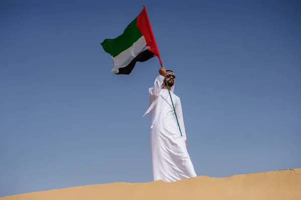 Orgulloso hombre árabe emiratí sosteniendo una bandera de los EAU en el desierto . — Foto de Stock