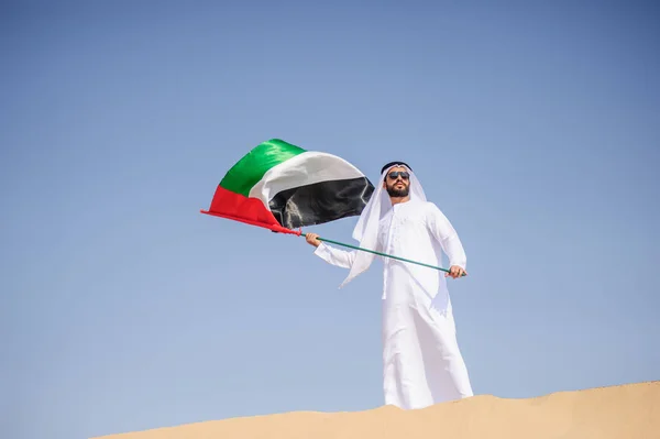 Orgulloso hombre árabe emiratí sosteniendo una bandera de los EAU en el desierto . — Foto de Stock