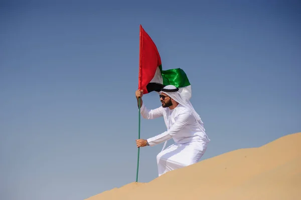 Orgulloso hombre árabe emiratí sosteniendo una bandera de los EAU en el desierto . — Foto de Stock