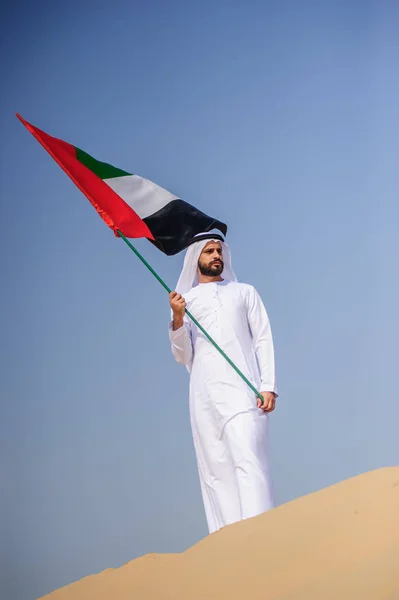 Orgulhoso homem Emirado árabe segurando uma bandeira dos Emirados Árabes Unidos no deserto . — Fotografia de Stock