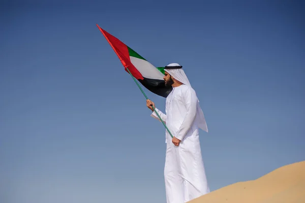 Orgulhoso homem Emirado árabe segurando uma bandeira dos Emirados Árabes Unidos no deserto . — Fotografia de Stock