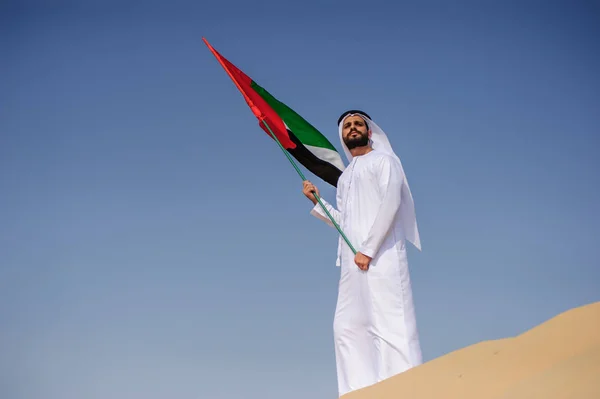 Orgulloso hombre árabe emiratí sosteniendo una bandera de los EAU en el desierto . — Foto de Stock