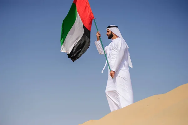 誇りに思ってアラビア首長人砂漠のアラブ首長国連邦の旗を保持しています。. — ストック写真