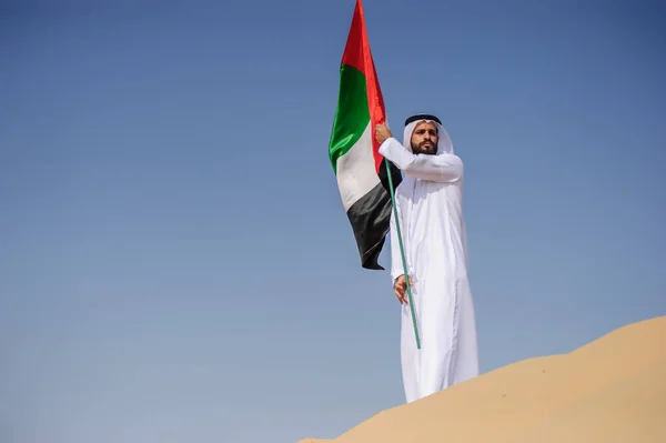 Orgulloso hombre árabe emiratí sosteniendo una bandera de los EAU en el desierto . — Foto de Stock