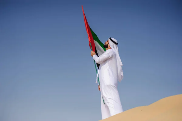 Orgulloso hombre árabe emiratí sosteniendo una bandera de los EAU en el desierto . — Foto de Stock