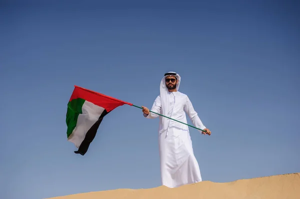 Orgulloso hombre árabe emiratí sosteniendo una bandera de los EAU en el desierto . — Foto de Stock