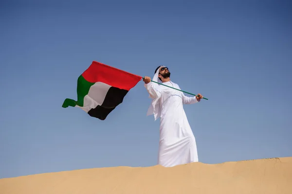 Orgulhoso homem Emirado árabe segurando uma bandeira dos Emirados Árabes Unidos no deserto . — Fotografia de Stock