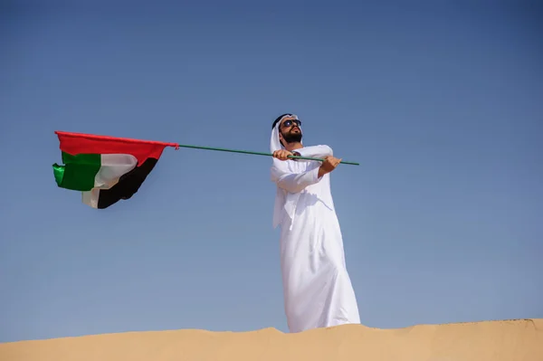 Orgulhoso homem Emirado árabe segurando uma bandeira dos Emirados Árabes Unidos no deserto . — Fotografia de Stock