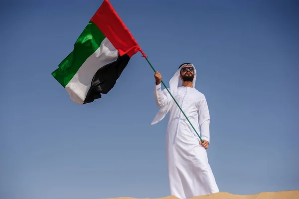 Orgulloso hombre árabe emiratí sosteniendo una bandera de los EAU en el desierto . — Foto de Stock