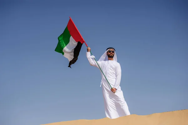 Orgulhoso homem Emirado árabe segurando uma bandeira dos Emirados Árabes Unidos no deserto . — Fotografia de Stock