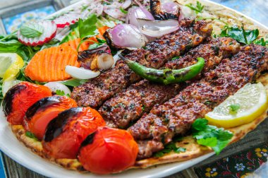 Sebzeli ve soslu sağlıklı barbekü. Siyah bir tabakla servis ediliyor. Işık arkaplanındaki görüntüyü kapat. Arapça yemek.