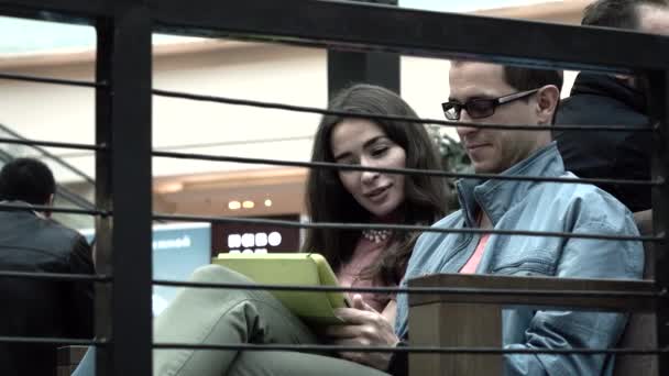 Bonita chica morena y hombre en gafas de borde negro usando tableta pc juntos en un café. Disparo 4K — Vídeo de stock