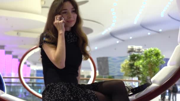 Beautiful young woman in black talking on her phone in a modern interior. 4K video — Stock Video