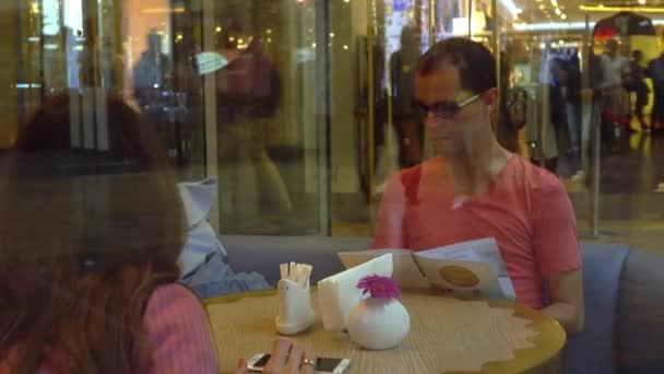 Oroszország, Moscow - szeptember, 13, 2016-ban. Pár egy modern bevásárlóközpont kávézóban nagy ablak mögé. Férfi és fiatal nő kiválasztásában étel. shot 4k — Stock videók