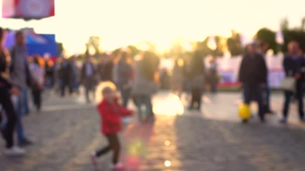Defokussierte Kind und die Eltern bei Sonnenuntergang in überfüllten Bereich. warme Farben. Zeitlupe Hintergrund Bokeh Clip — Stockvideo
