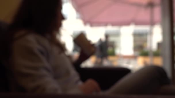 Chica morena desenfocada tomando su copa con una paja en un café junto a la ventana. Fondo de cámara lenta bokeh disparo — Vídeos de Stock