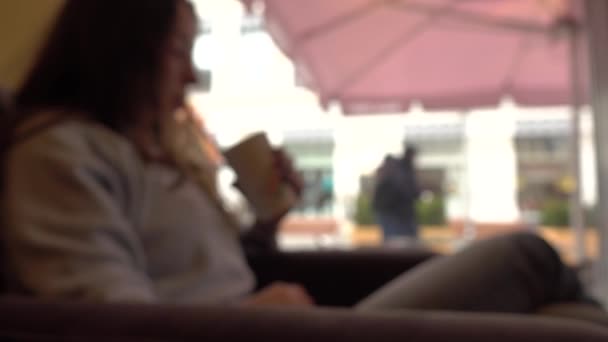 Расплывчатая брюнетка выпивает с соломинкой в кафе у окна. 4K фоновый боке клип — стоковое видео
