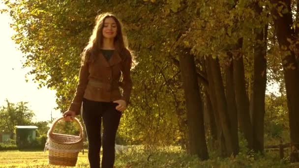 Slow motion steadicam video of a beautiful girl in brown jacket walking through autumn forest carrying a basket — Stock Video