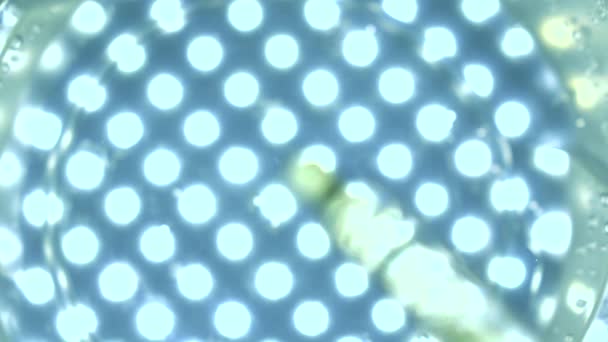 Tropfendes Öl im Wasser gegen mehrere Scheinwerfer blauen Hintergrund. chemische Experiment-Konzept. Zeitlupenvideo — Stockvideo