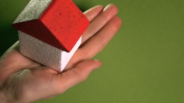 Woman holding toy house with red roof against green background. Real estate agent concept. 4K shot — Stockvideo