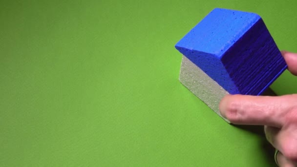 Ріелтор розміщує іграшковий будинок з синім дахом і невеликим ключем на зеленому тлі. Концепція угоди про нерухомість. 4K постріл — стокове відео