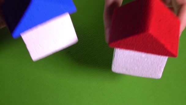 Real estate agent placing toy houses with red and blur roofs against green background. Development concept. 4K video — Αρχείο Βίντεο