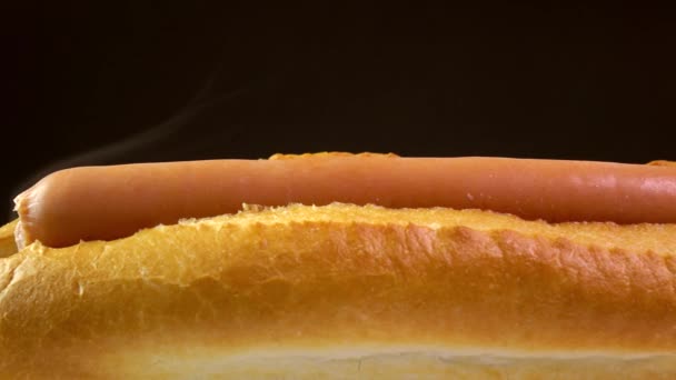 Tomatensauce auf Hot Dog vor schwarzem Hintergrund. weltweit beliebtes Fast Food. 4k Nahaufnahme Dolly-Video — Stockvideo