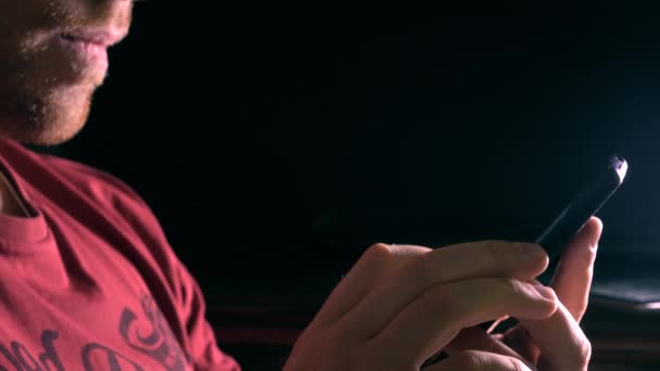 Молодий бородатий чоловік використовує свій смартфон у темній кімнаті відео 4K. Вільний простір для інфографіки або підписів — стокове відео