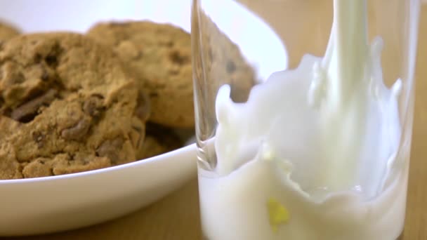 Шоколадное печенье и молоко, наливаемое в стакан. 4К крупным планом супер медленный снимок — стоковое видео