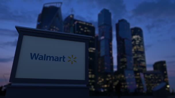 Placa de sinalização de rua com logotipo Walmart à noite. Desfocado arranha-céus distrito de negócios fundo. Editorial 4K clip — Vídeo de Stock