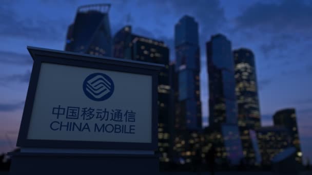 Tablero de la señalización de calle con el logotipo móvil de China en la noche. Rascacielos distritos de negocios borrosa fondo. Clip editorial 4K — Vídeos de Stock