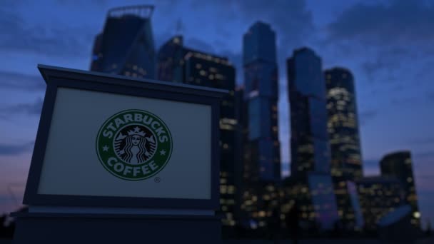 Gatan skyltar ombord med Starbucks logotyp på kvällen. Suddig business district skyskrapor bakgrund. Redaktionella 4k klipp — Stockvideo