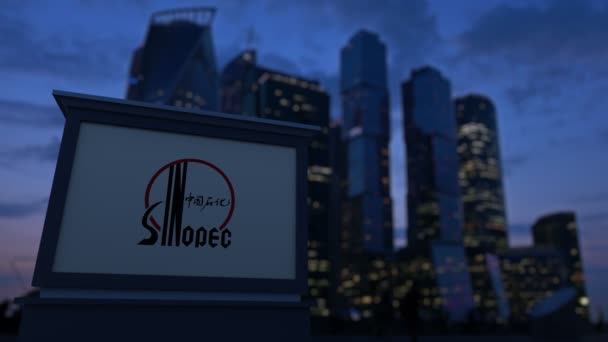 Уличная вывеска с логотипом Sinopec вечером. Размытые данные о небоскребах в деловом районе. Клип в 4K — стоковое видео