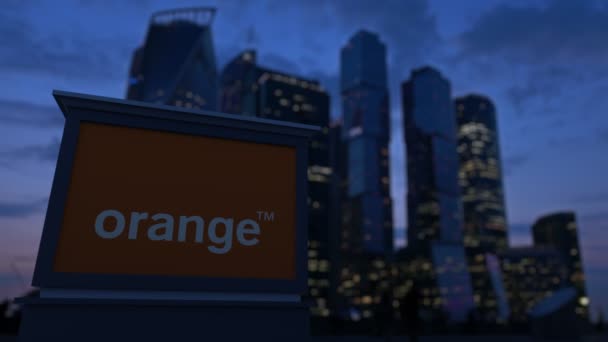 Panneau de signalisation avec logo Orange S.A. dans la soirée. Fond flou de gratte-ciel de quartier d'affaires. Clip éditorial 4K — Video