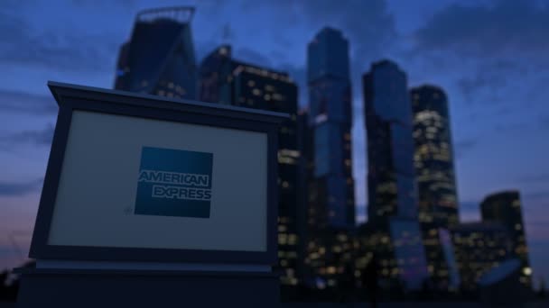 Panneau de signalisation avec logo American Express dans la soirée. Fond flou de gratte-ciel de quartier d'affaires. Clip éditorial 4K — Video