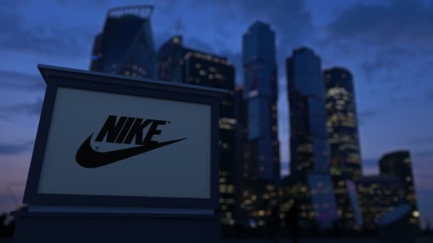 Cartelera con inscripción Nike y logo en la noche. Rascacielos distritos de negocios borrosa fondo. Clip editorial 4K — Vídeos de Stock